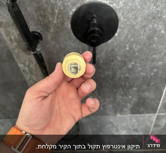 יד מחזיקה חלק צנרת מול קיר אמבטיה